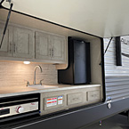Camp kitchen with pull-out griddle , sink, mini refrigerator, drawers, and overhead cabinets
 May Show Optional Features. Features and Options Subject to Change Without Notice.