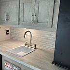 Close-up of camp kitchen sink and overhead cabinets
 May Show Optional Features. Features and Options Subject to Change Without Notice.